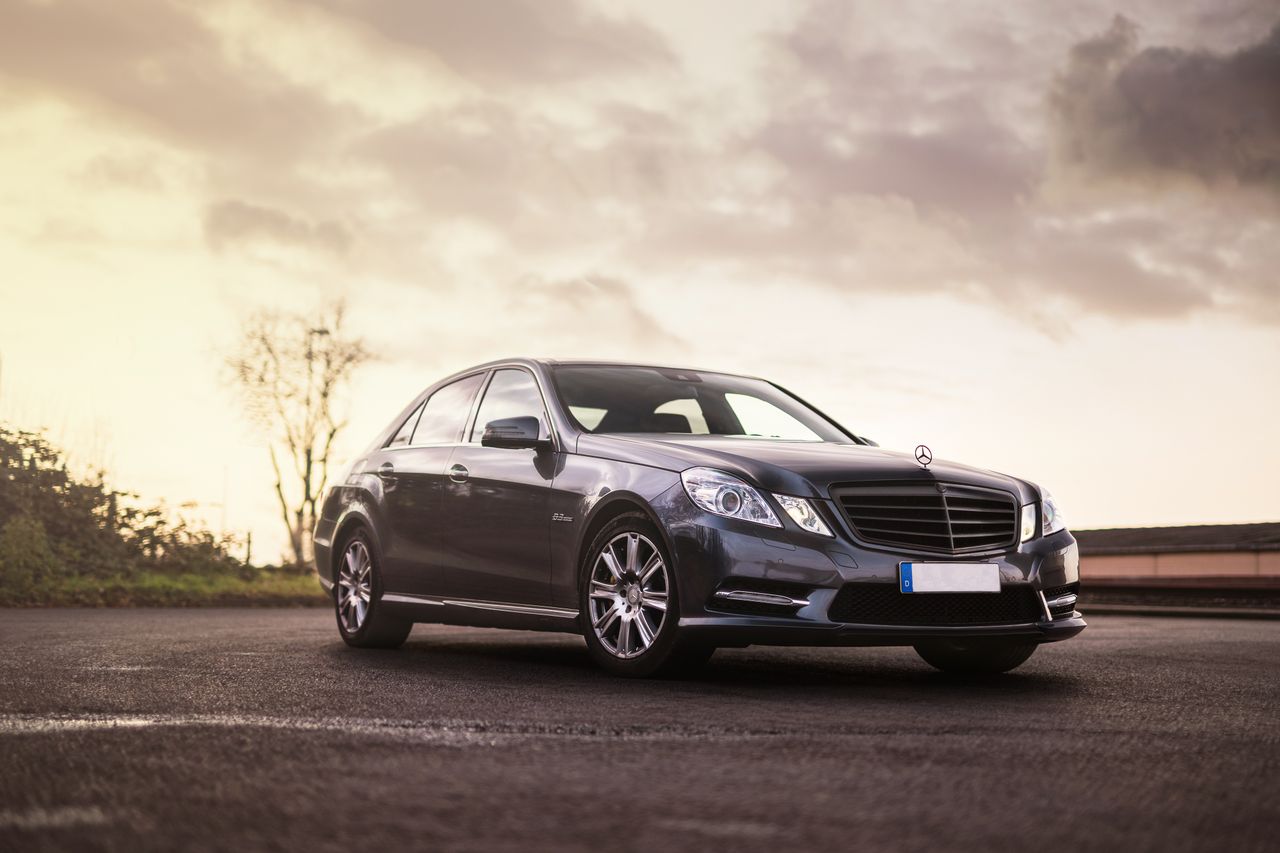 Elegant black sedan in scenic outdoor setting during sunset with dramatic cloudscape.